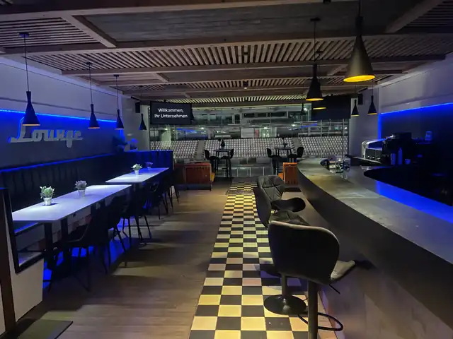 Innenansicht der Lounge mit Sitzplätzen, Bar und Blick auf die Rennstrecke.