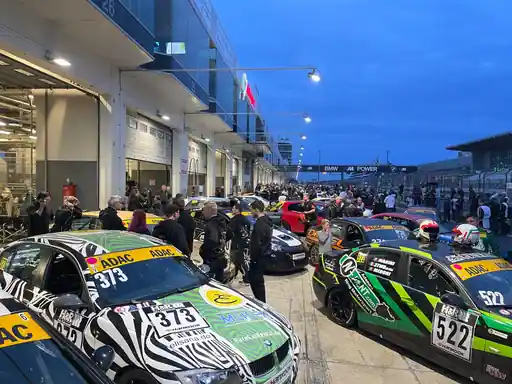 Rennfahrzeuge mit Sponsorenlogos in der Nürburgring-Boxengasse.
